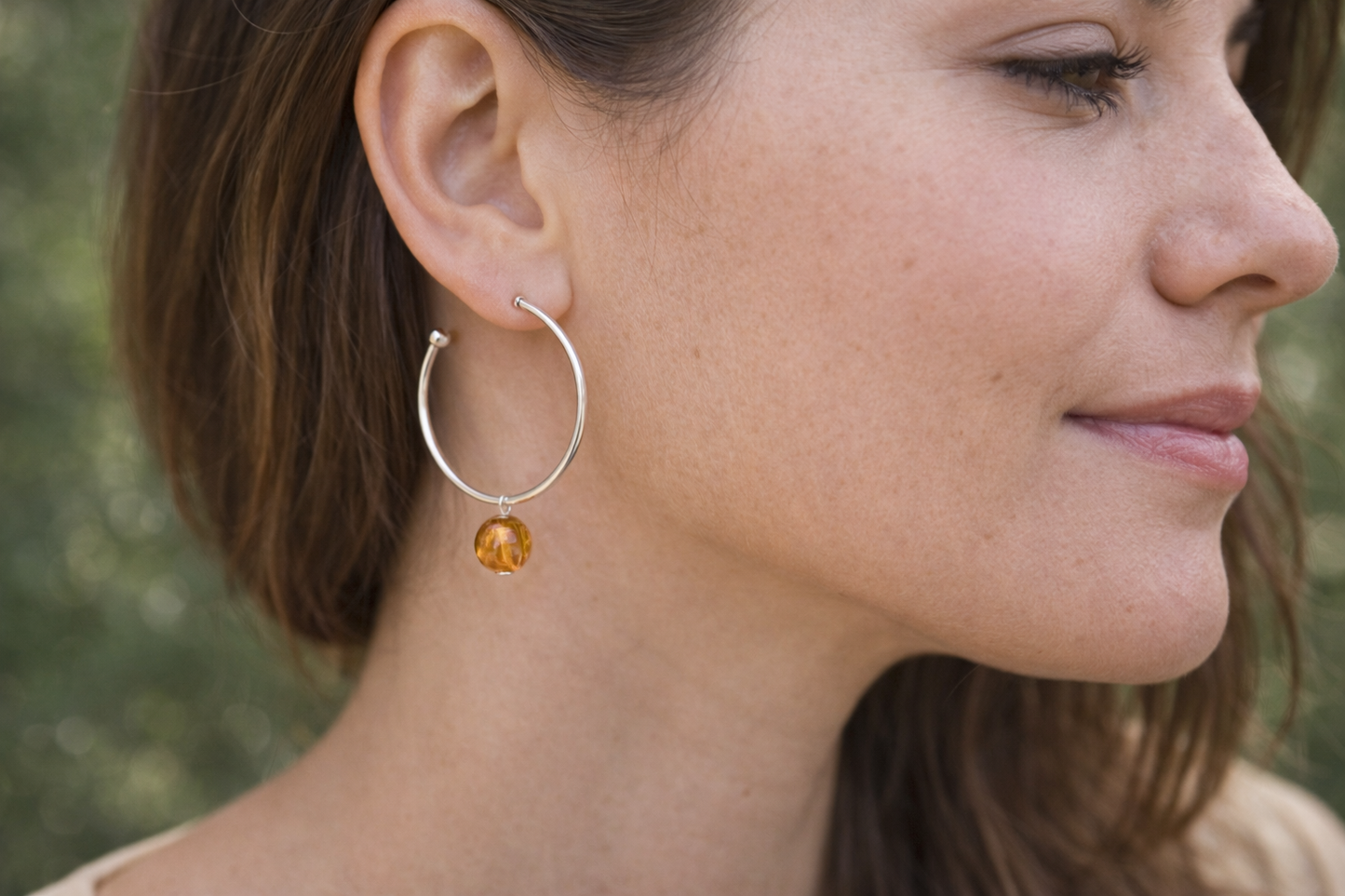 Close-up of a woman wearing a hoop earring with a small round pendant.