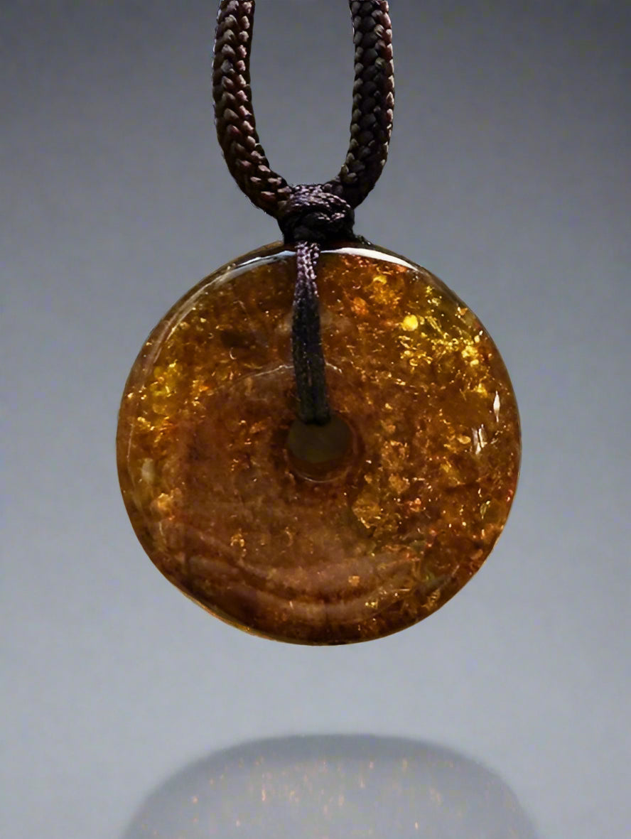 Round amber pendant on a chain against a textured beige background