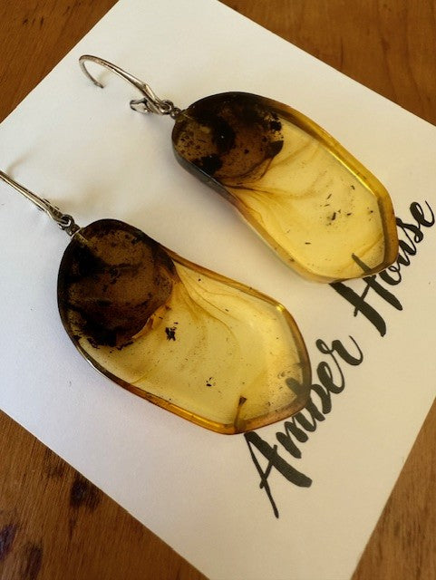 A pair of teardrop-shaped amber earrings placed on a piece of paper with the name 'Amber House' written on it.