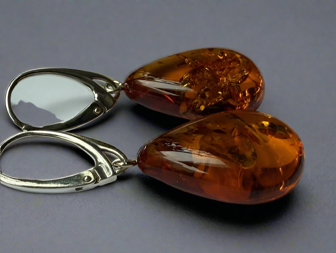 A pair of teardrop-shaped amber earrings with sterling silver finish, displayed against a grey background.
