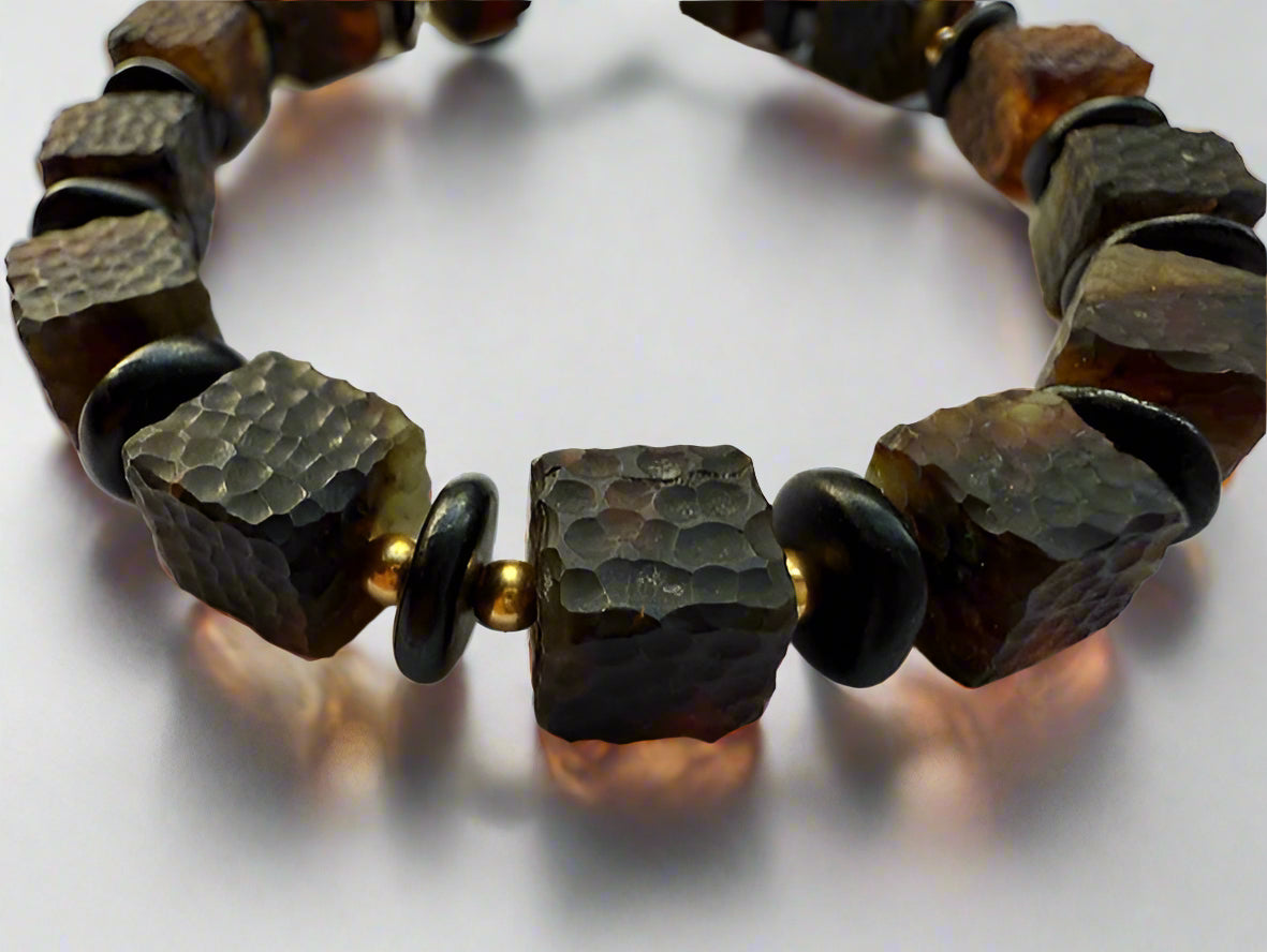 A close-up image of a textured amber cube bracelet with smooth, rounded beads of a dark, contrasting stone, showcasing the bracelet's detailed craftsmanship and the natural translucent quality of the amber.