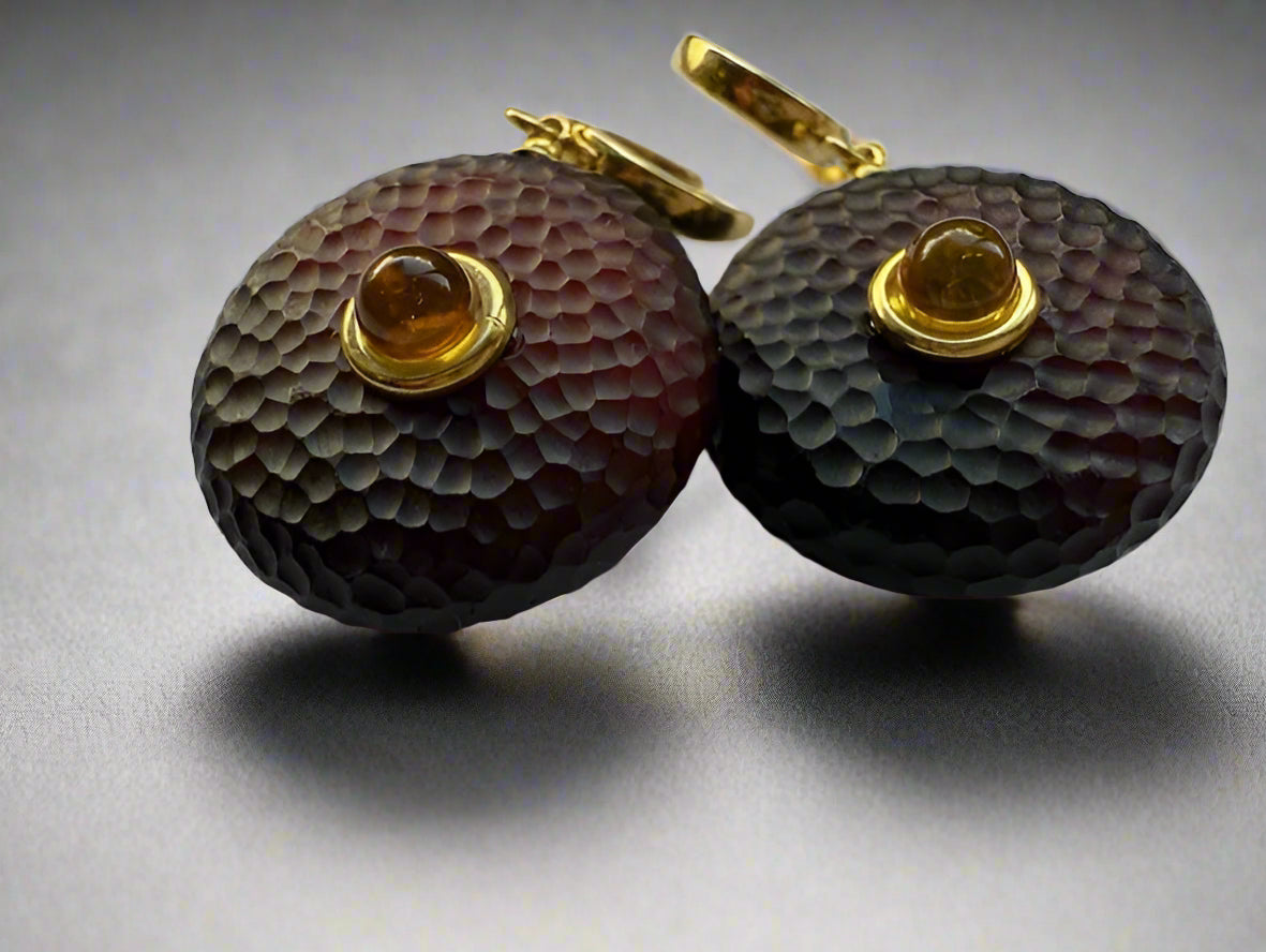 A pair of round amber earrings with honeycomb texture and a central smooth cabochon, suspended from gold ear wires.
