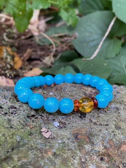 A turquoise and amber bracelet with blue beads and two honey amber beads, displayed on a rock.