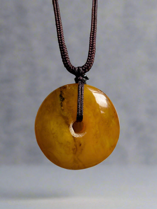 Round amber pendant on a string against a textured beige background