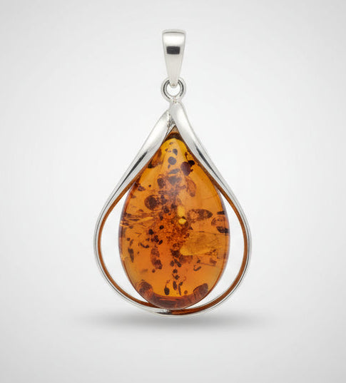 Teardrop-shaped amber pendant in a silver setting on a wooden surface