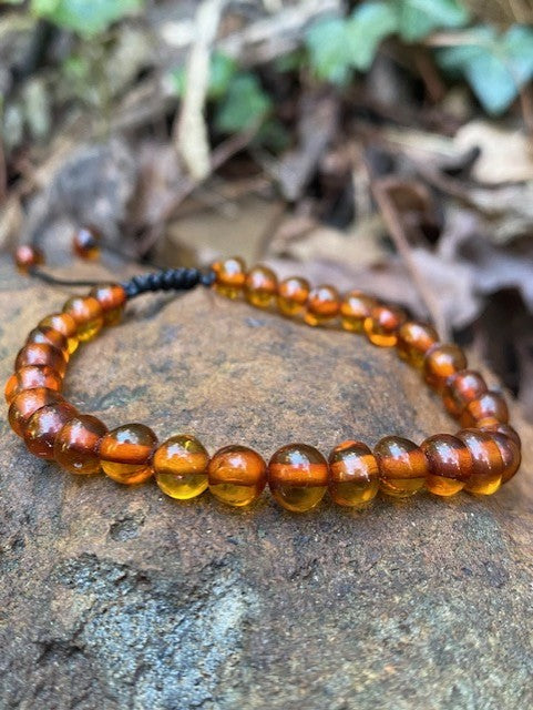 A cognac amber bracelet with adjustable black string, displayed on a natural outdoor background.