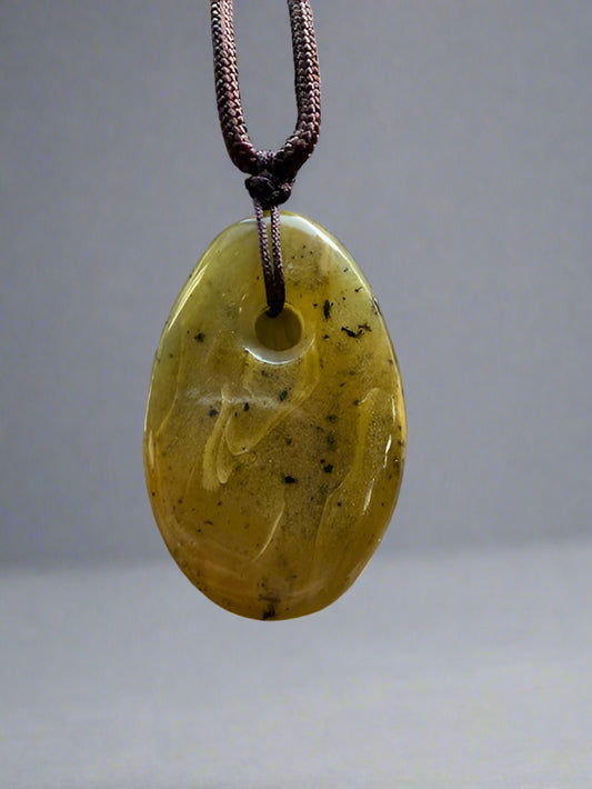Yellow jade pendant on a dark cord against a gray background