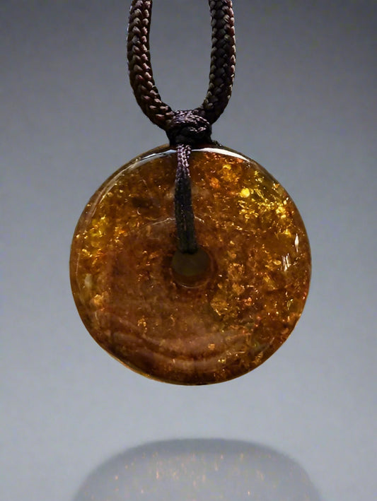 Round amber pendant on a chain against a textured beige background