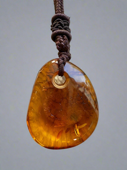 Amber teardrop pendant on a string against a textured beige background