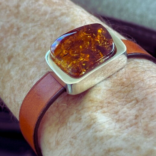 A man's wrist wearing a leather bracelet with a sterling silver bezel and amber stone.