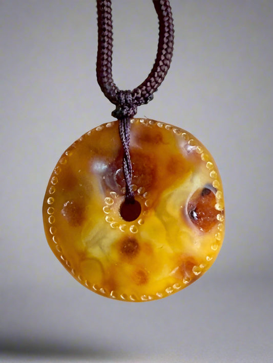 Round amber-colored pendant on a string against a beige background