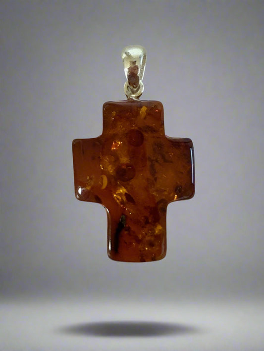 Amber cross pendant with silver setting on a light gray background