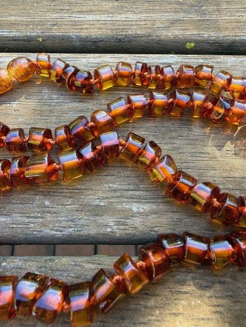 Three amber-colored beaded necklaces on a wooden surface