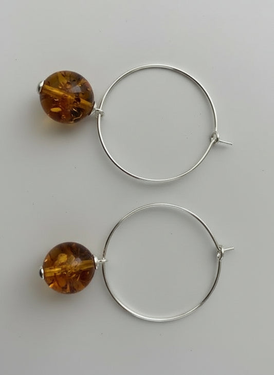 Silver hoop earrings with amber beads on a textured surface