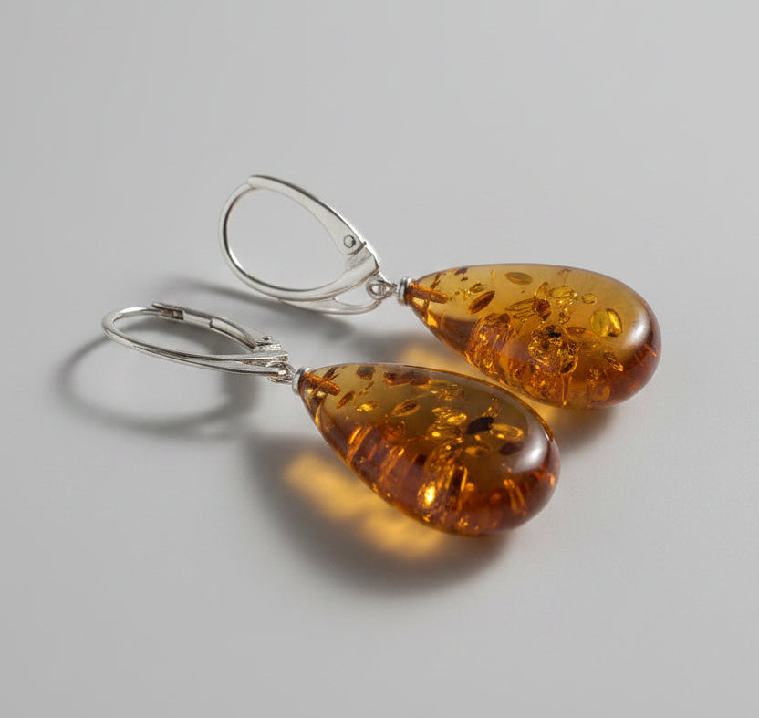 Amber teardrop earrings with silver hooks on a light gray surface.