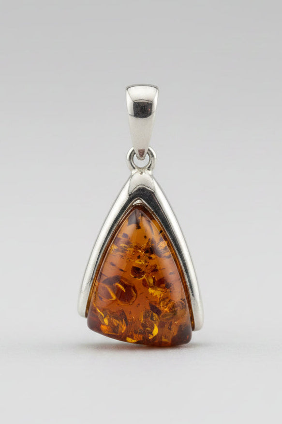 A triangular amber pendant in a silver bezel setting, displayed on a textured off-white surface.