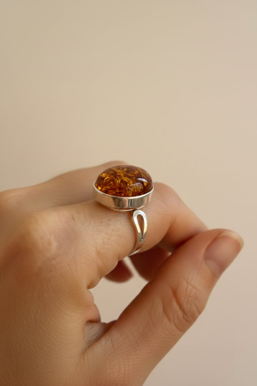 Hand wearing a silver ring with a amber stone on a beige background