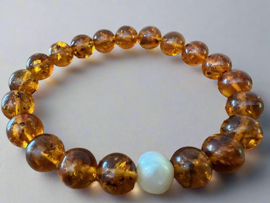 A bracelet with round honey amber beads and one white baroque pearl
