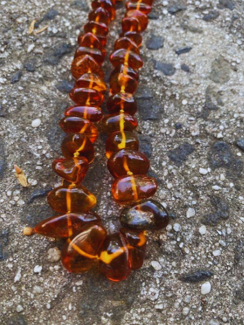 A cognac brown amber necklace laid out on a textured surface.