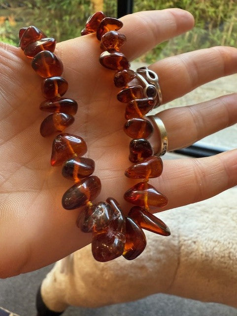 Hand wearing a bracelet with amber beads and two rings.