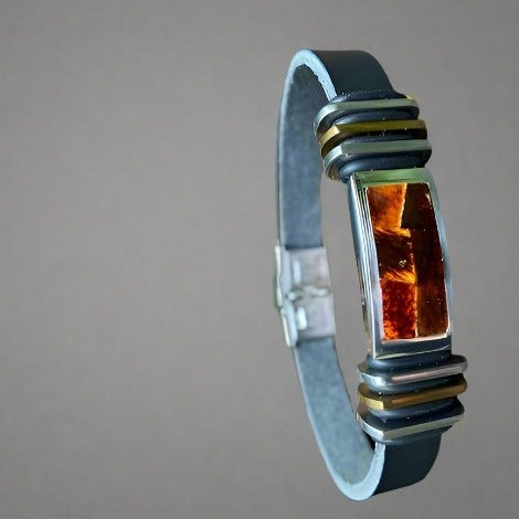 A men's leather bracelet with a cognac amber color inset and stainless steel clasp.