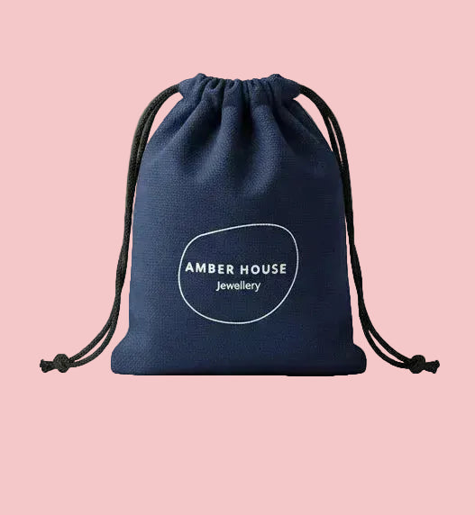 Blue drawstring pouch with 'Amber House Jewelry' logo on a wooden surface