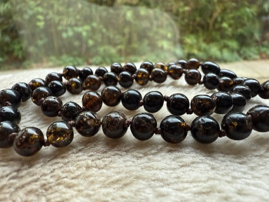 Necklace of dark amber beads on a textured surface with a blurred natural background
