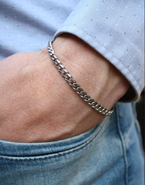A man's wrist wearing a silver chain bracelet with a lobster clasp closure.