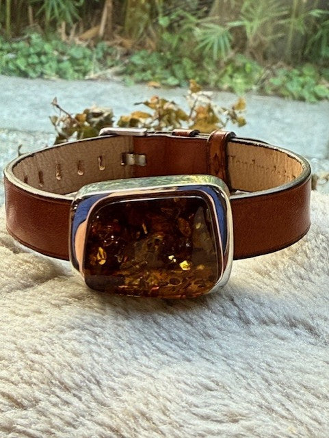 Brown leather bracelet with amber accent on a textured surface.