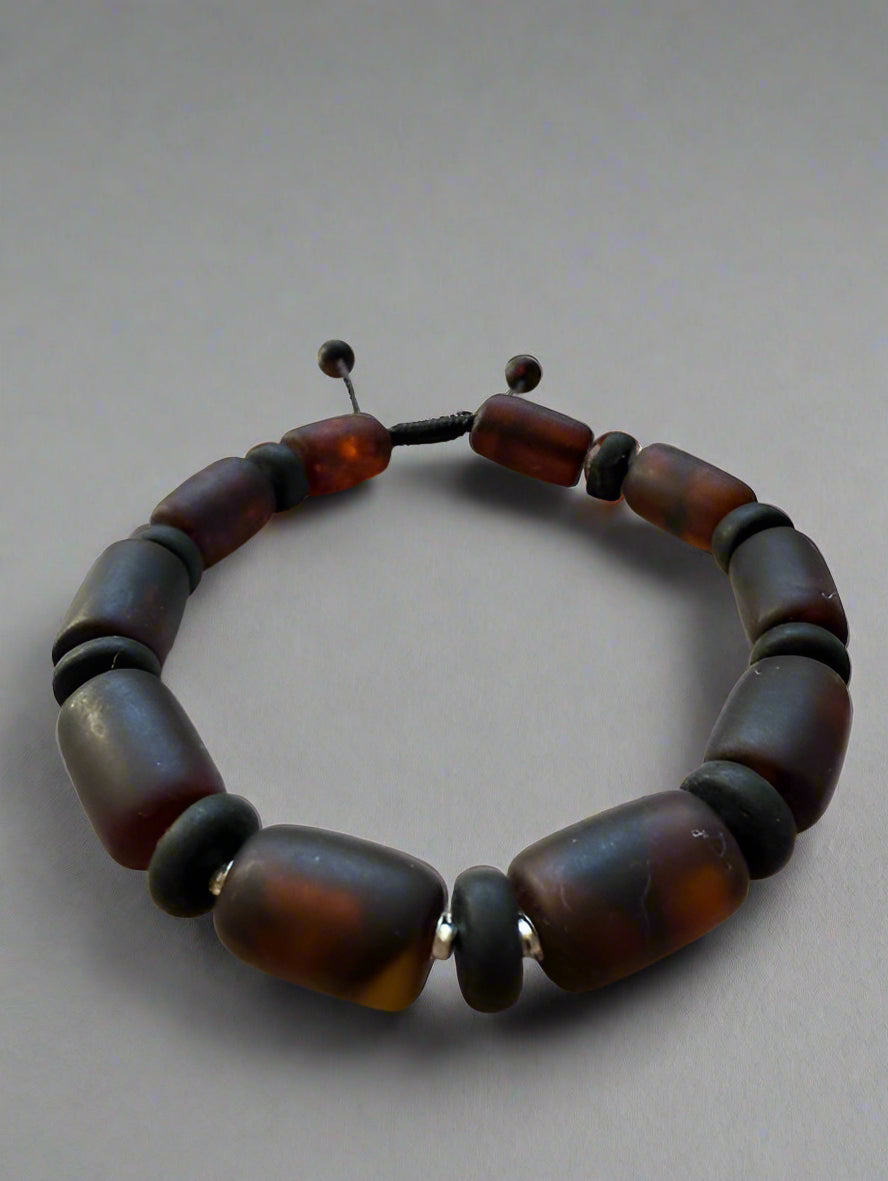 Bracelet with brown and black beads on a textured surface with a blurred natural background