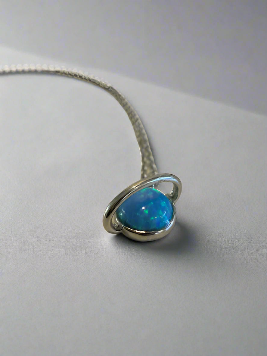 Blue opal pendant on a chain against a neutral background