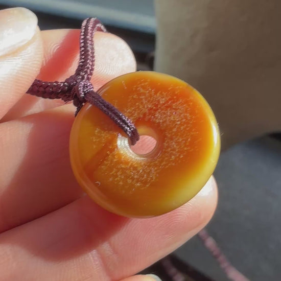 Round amber-colored pendant on a brown cord against a textured beige background video 