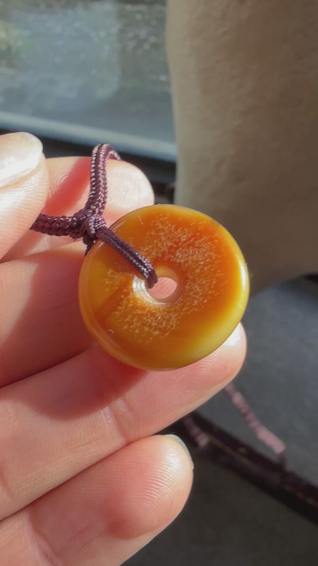 Round amber-colored pendant on a brown cord against a textured beige background video 