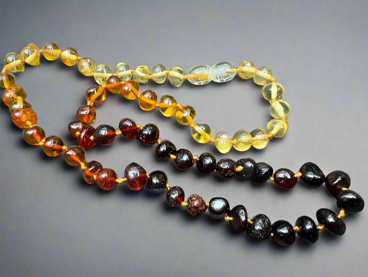 Three amber necklaces of different colours on a stone surface
