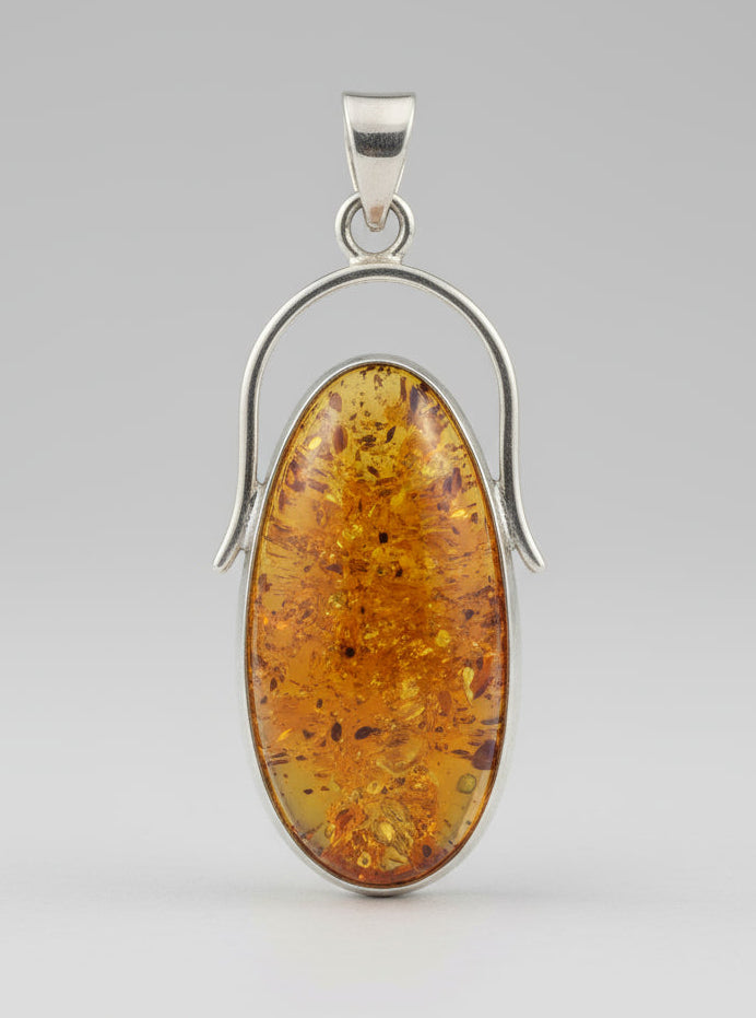 Amber pendant with silver setting held in a hand against a dark background
