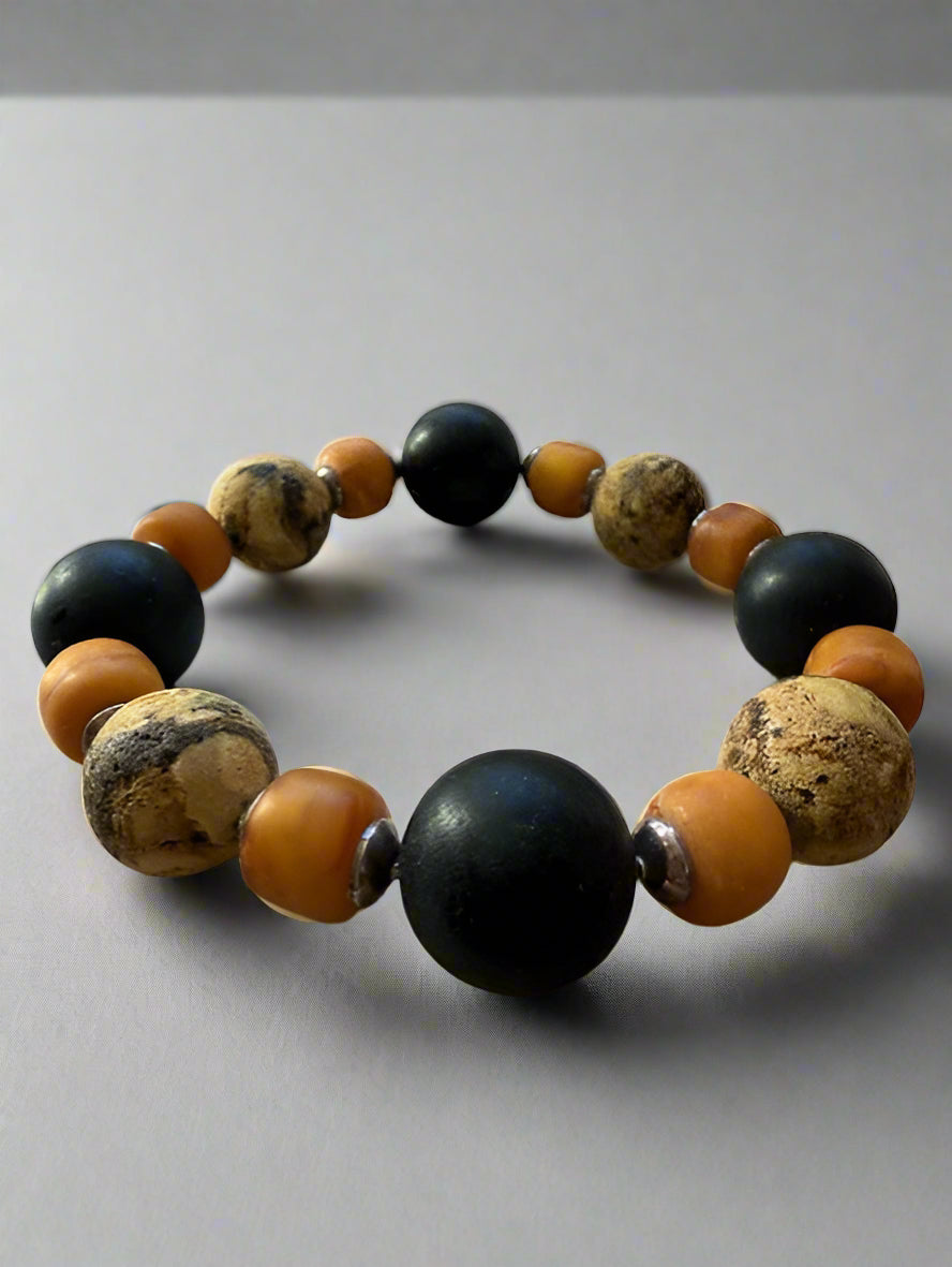 Bracelet with black, orange, and brown beads on a textured surface with a blurred natural background
