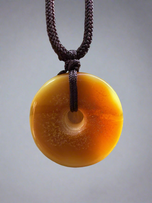 Round amber-colored pendant on a brown cord against a textured beige background
